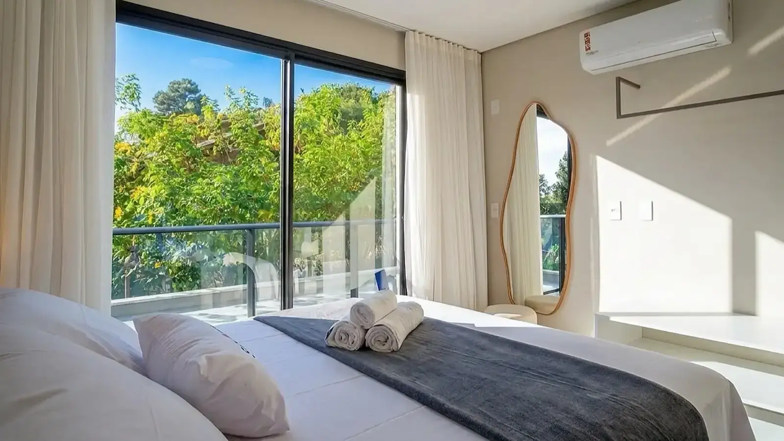 Quarto com cama arrumada e porta de vidro aberta para a vegetação da Praia do Rosa